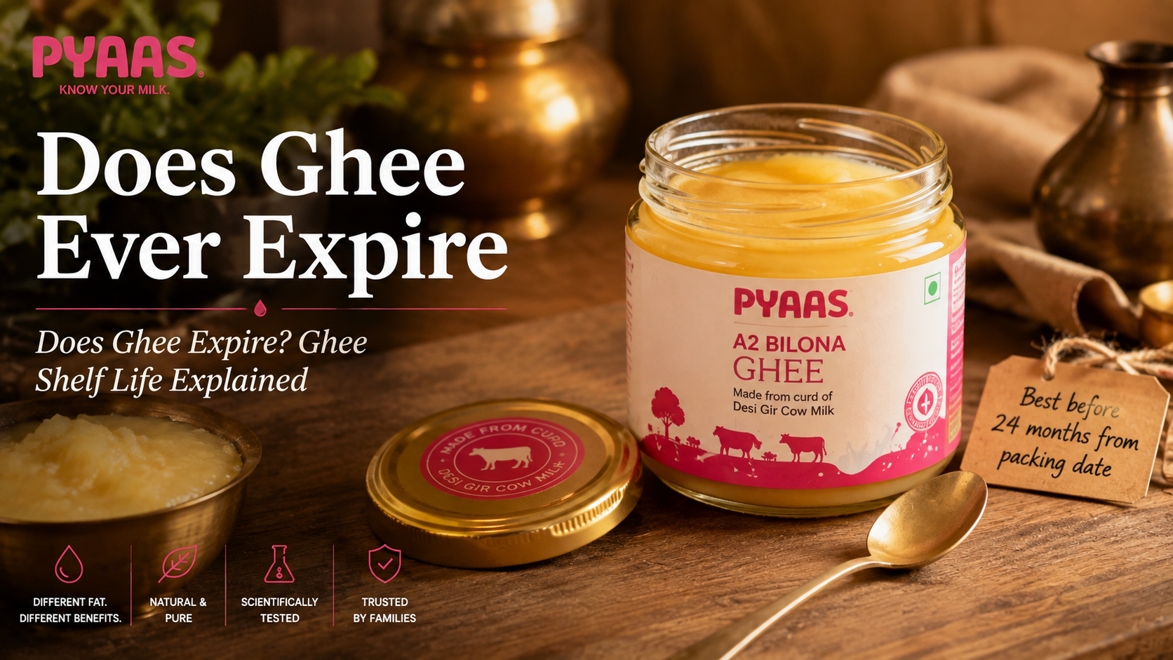 An open glass jar of golden PYAAS A2 ghee with a clean spoon and a small best-before tag on a wooden surface.